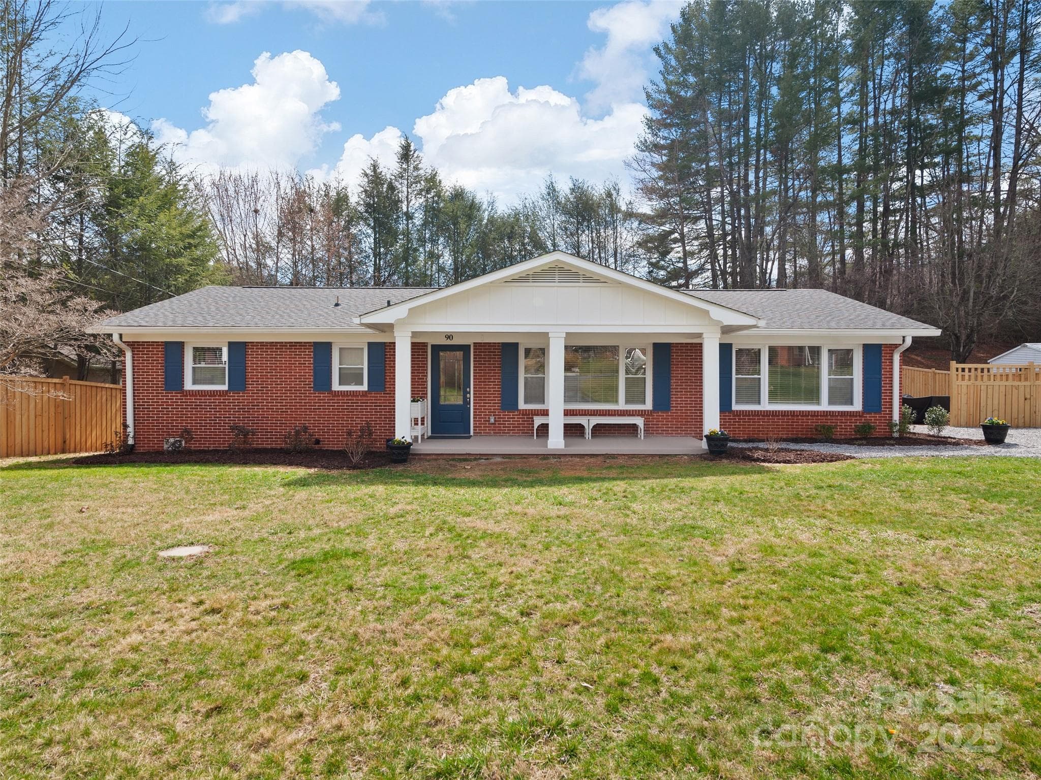 One-story red brick ranch house with blue shutters and a white gabled front porch.