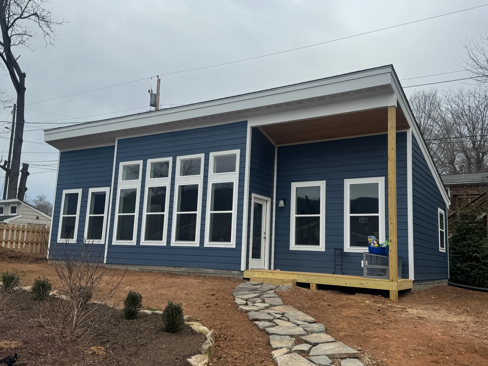 Modern blue house with white trim, large windows, and a stone path on dirt.