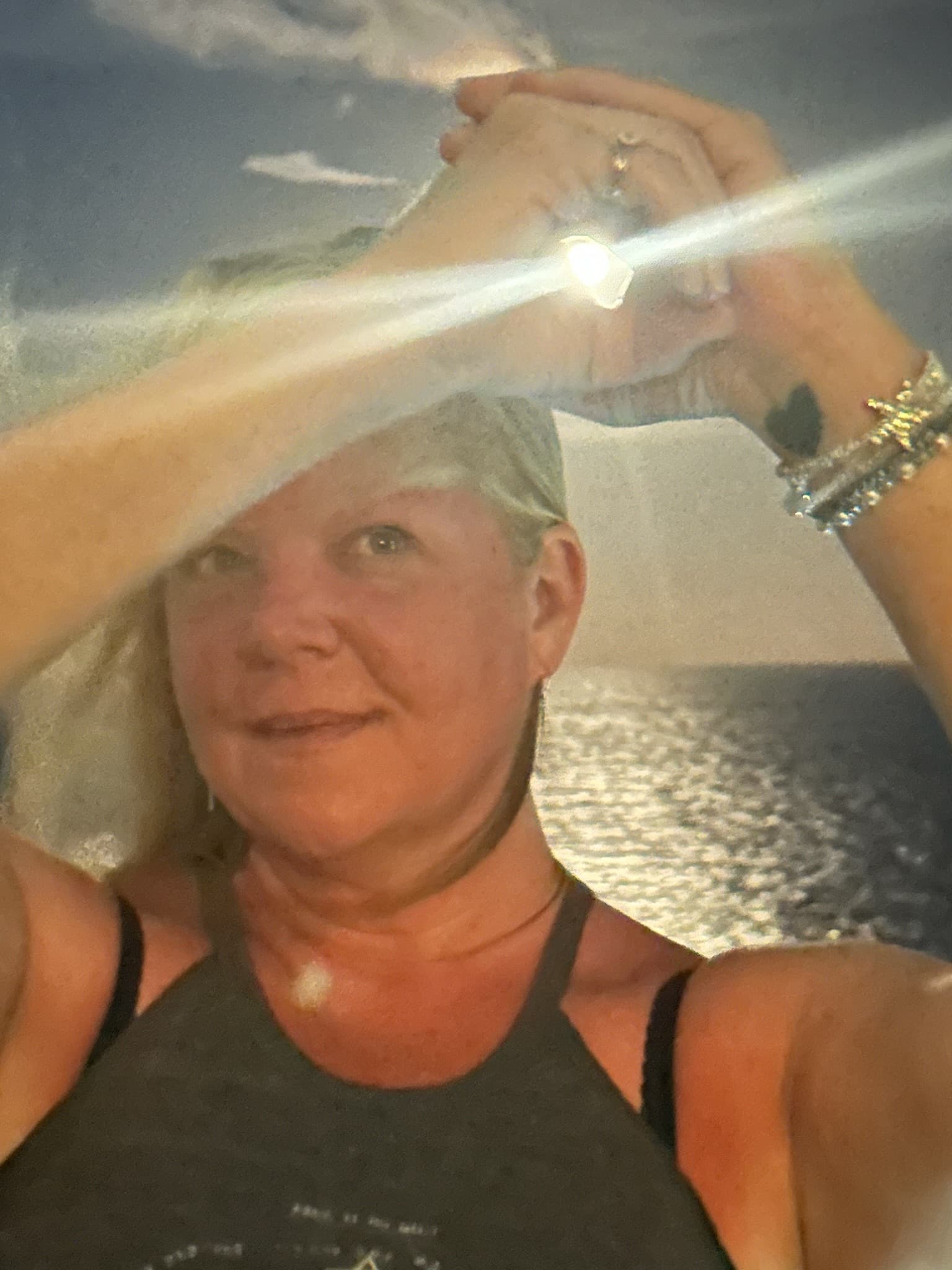 Blonde woman holding a bright light between her hands against a shimmering ocean background.